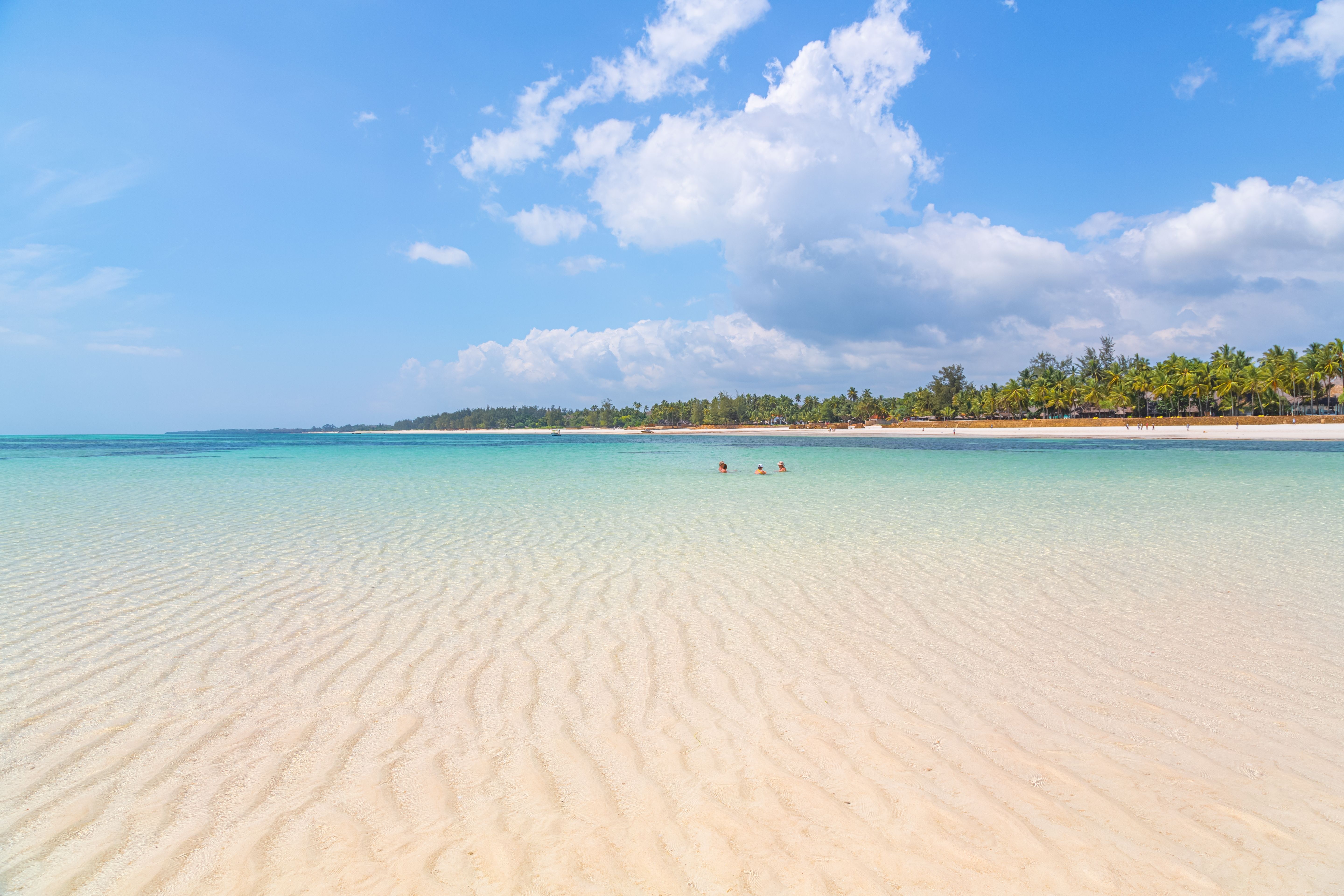Det smukke hav glitrer i solen, mens mennesker svømmer og nyder bølgerne på en varm dag » Tembo Travel Det smukke hav glitrer i solen, mens mennesker svømmer og nyder bølgerne på en varm dag