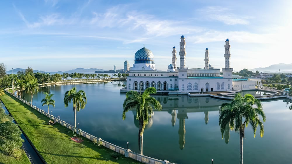Luftfoto af Kota Kinabalu by og den flydende moské i Sabah, Borneo – moderne bylandskab kombineret med ikonisk arkitektur og kystmiljø.