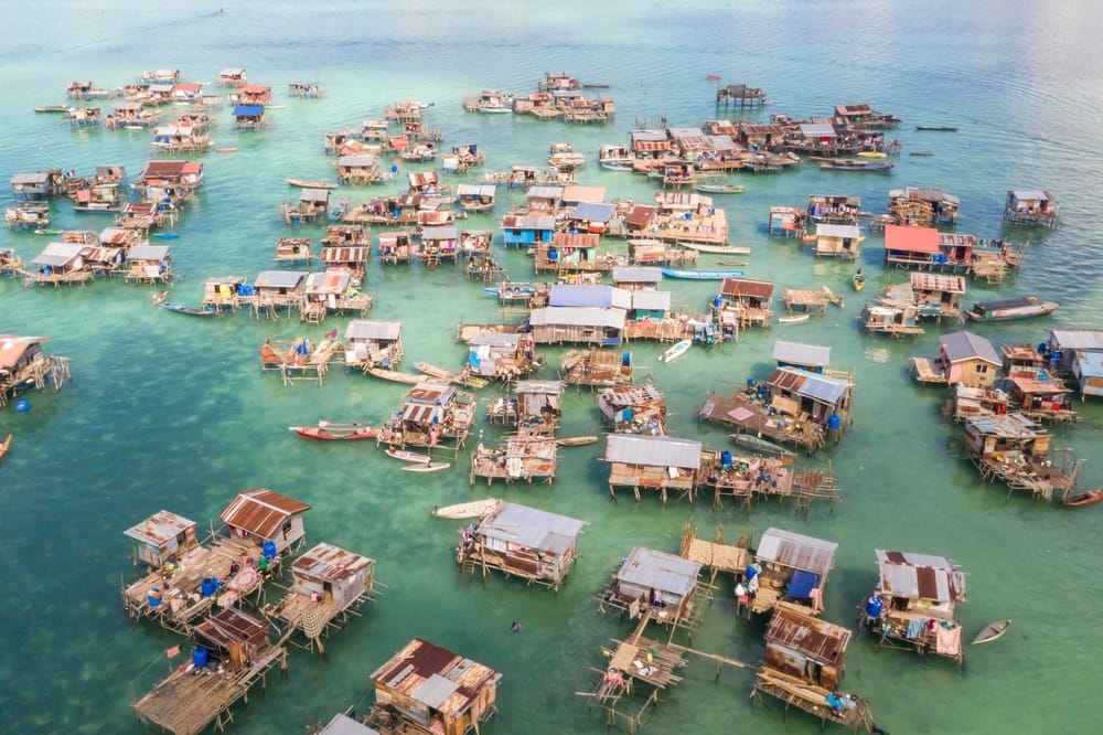 Luftfoto af Borneo Sea Gypsy-vandsby på Omadal, Malaysia – traditionelle husbåde i tropisk kystmiljø omgivet af klart vand.