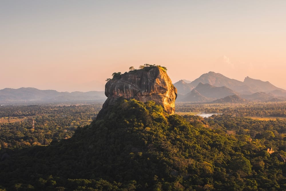Sigiriya Rock, også kendt som Løveklippen, badet i gyldent lys ved solnedgang. Den ikoniske klippefæstning i Sri Lanka rejser sig majestætisk over junglen og er et UNESCO-verdensarvssted med ruiner, fresker og en enestående udsigt.