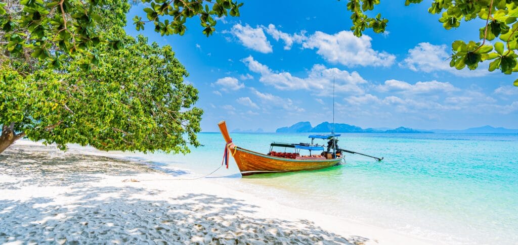 Hav og sandstrand med traditionelle longtail-både på stranden – idyllisk tropisk kystscene med klart vand og palmer. » Tembo Travel Hav og sandstrand med traditionelle longtail-både på stranden – idyllisk tropisk kystscene med klart vand og palmer.