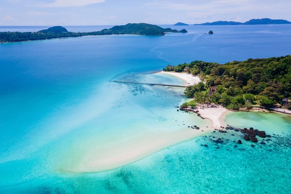 Luftfoto af Koh Kham Island i Trat, Thailand. Den idylliske strand med hvidt sand, turkisblåt hav og små sorte vulkanske klipper skaber et tropisk paradis – perfekt for rejsende, der søger ro, snorkling og naturoplevelser.