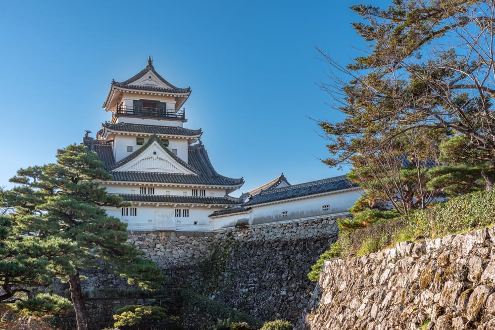 Kochi-slottet rejser sig majestætisk med sine hvide mure og mørke trækonstruktioner, omgivet af frodig natur i Kochi, Japan.