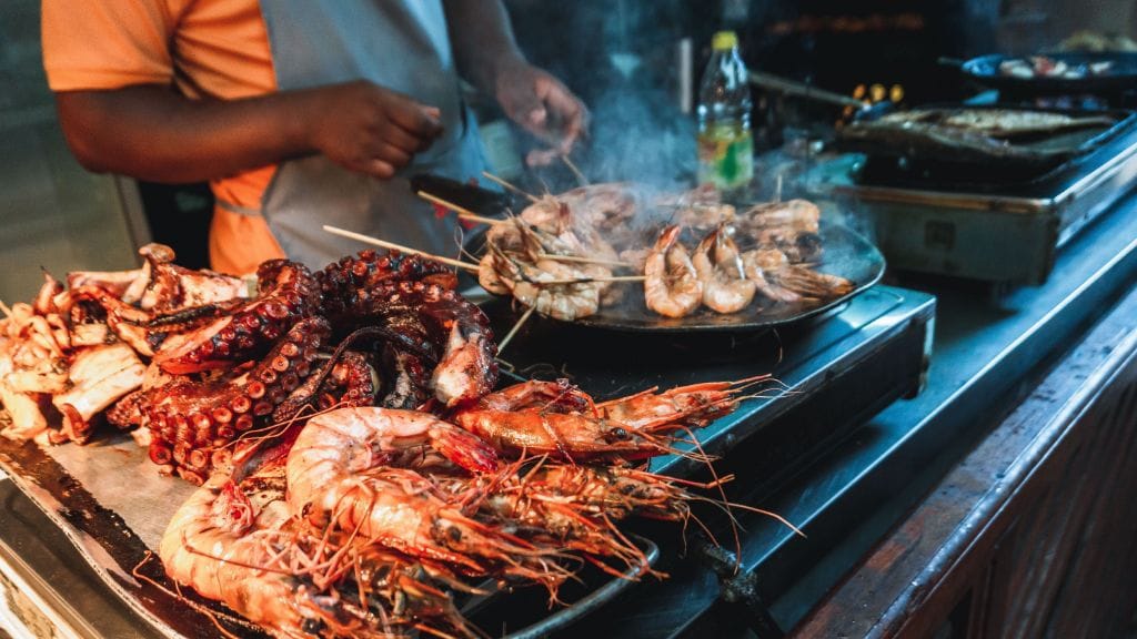 En lokal mand forbereder friskfanget seafood i Stone Town, hjertet af Zanzibar, kendt for sit livlige madmarked og kystens kulinariske traditioner.