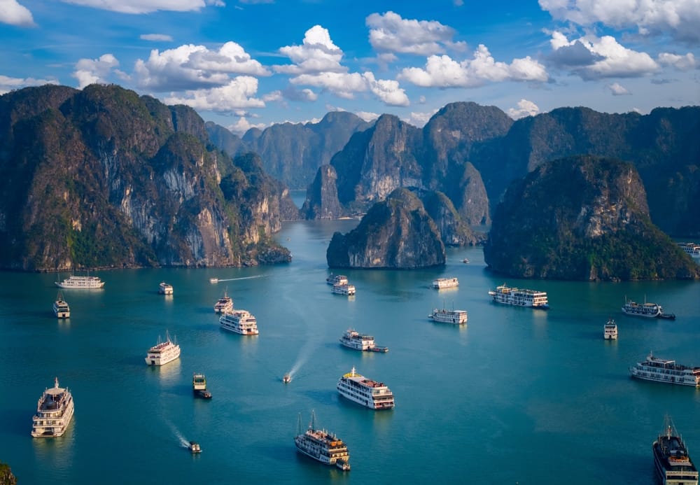 Luftfoto af Halong Bay, hvor både sejler mellem majestætiske kalkstensøer, der rejser sig dramatisk fra det turkisgrønne hav.