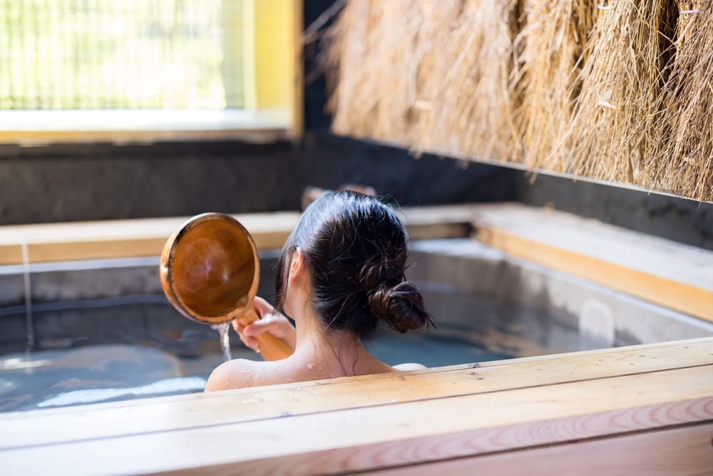 Asiatisk kvinde nyder et afslappende bad i en traditionel japansk onsen, omgivet af dampende varmt kildevand