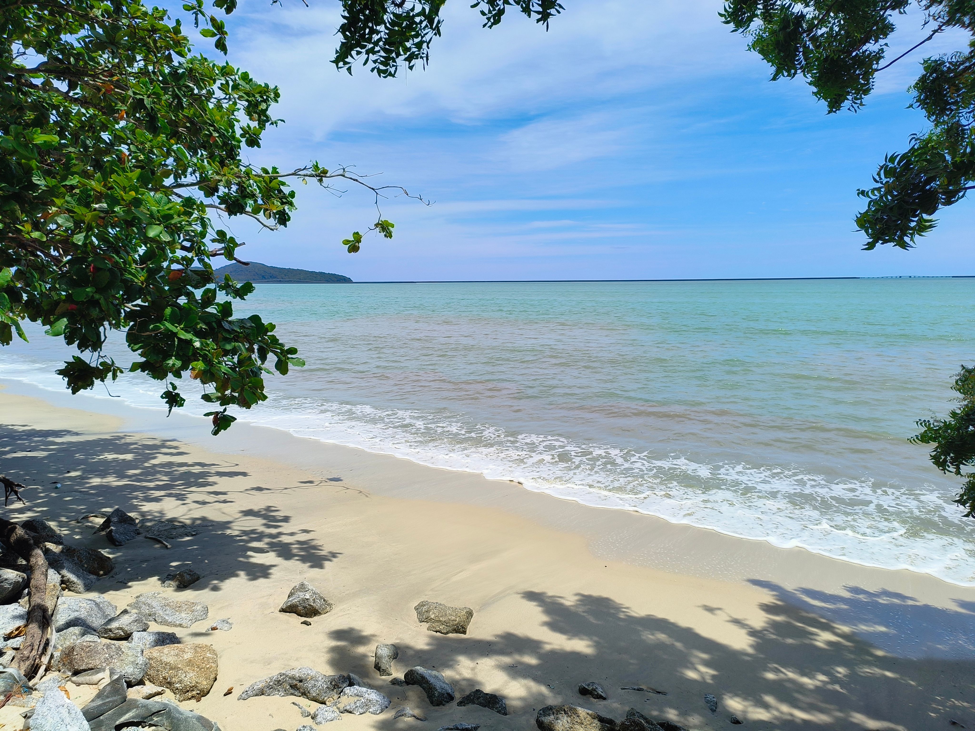 Smuk strand nær Pantai Cenang på Langkawi, Malaysia, med hvidt sand, klart vand og palmer langs kysten