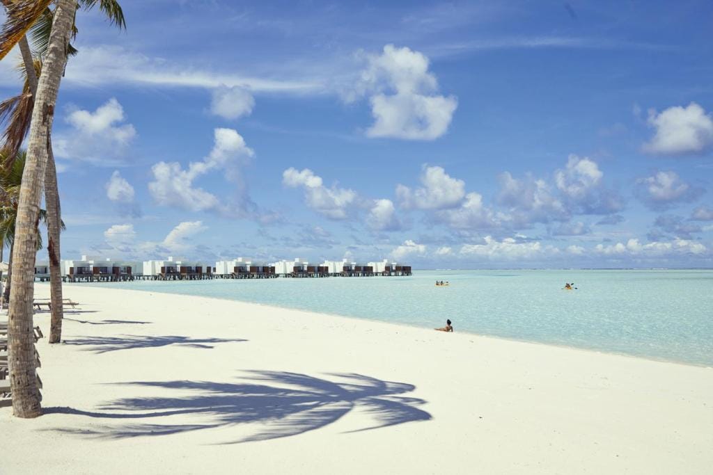 Hvid sandstrand på RIU Atoll med turkis vand og overwater villas i baggrunden.