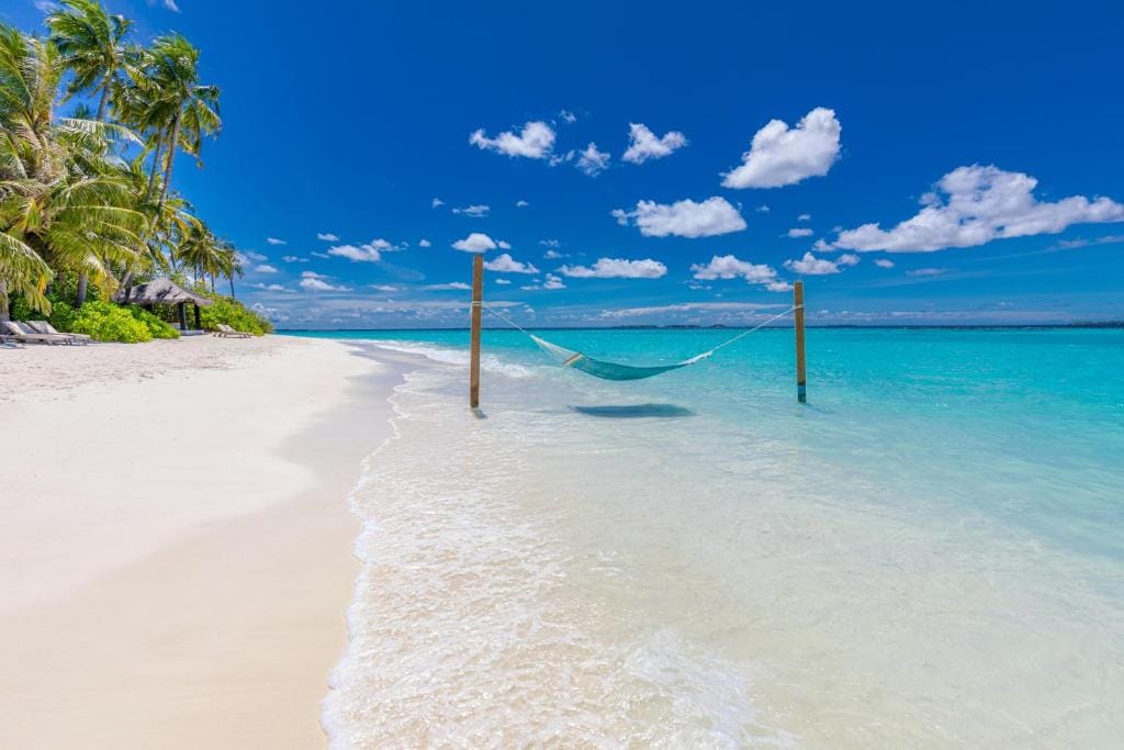 Hængekøje over det turkisblå hav ved den hvide sandstrand på Sun Siyam Iru Fushi, Maldiverne.