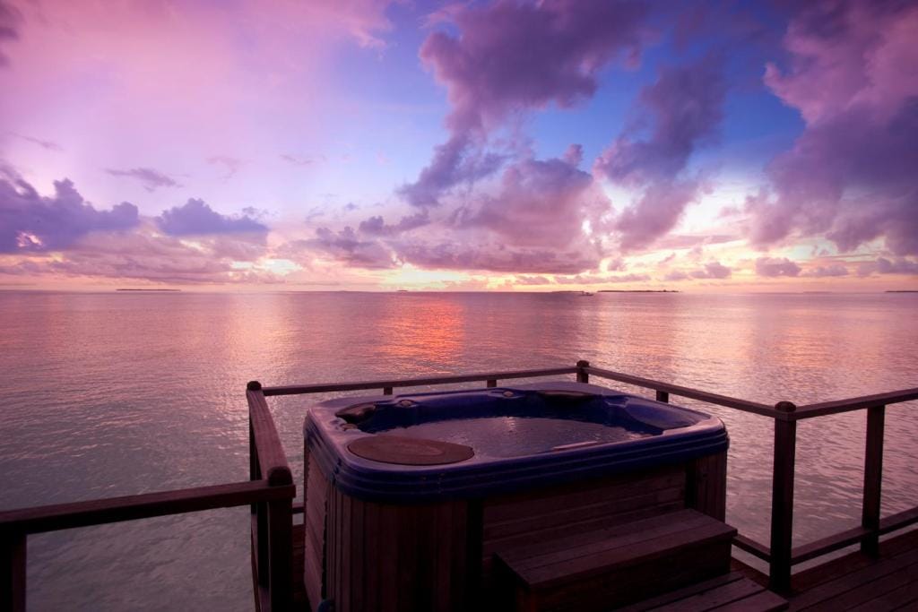 Jacuzzi over havet på Sun Siyam Iru Fushi med udsigt til farverig solnedgang.