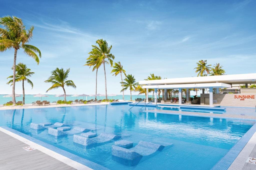 Poolområde på RIU Atoll med palmer, solsenge og havudsigt.