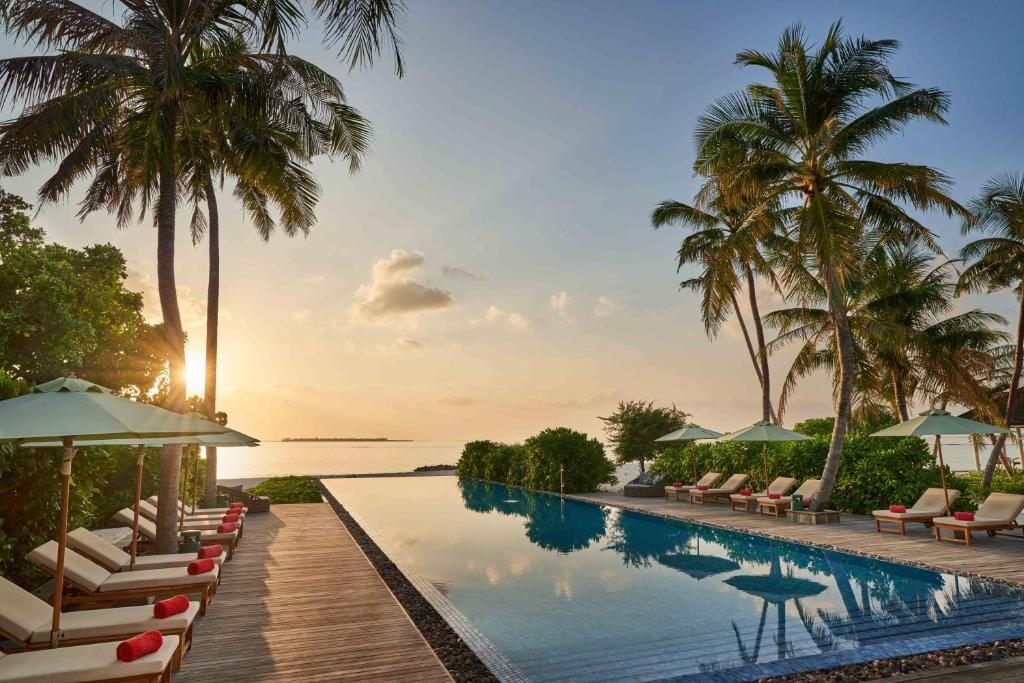 Poolområde på Siyam World på Maldiverne med palmer, solsenge og solnedgang over havet.Poolområde på Siyam World på Maldiverne med palmer, solsenge og solnedgang over havet.