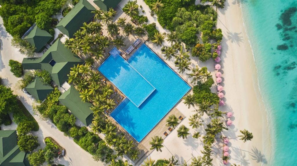 Luftfoto af Siyam Worlds poolområde på Maldiverne med palmer, strand og turkisblåt hav.