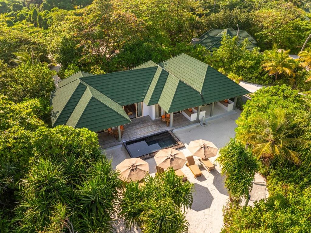 Luftfoto af en strandvilla på Siyam World på Maldiverne omgivet af tæt, grøn vegetation og terrasse med parasoller.