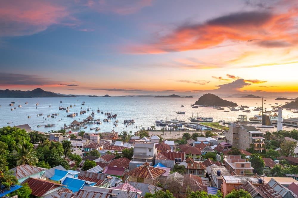 Panoramisk udsigt over Labuan Bajo havn, Flores, Indonesien, med både, øer og gyldent aftenlys.