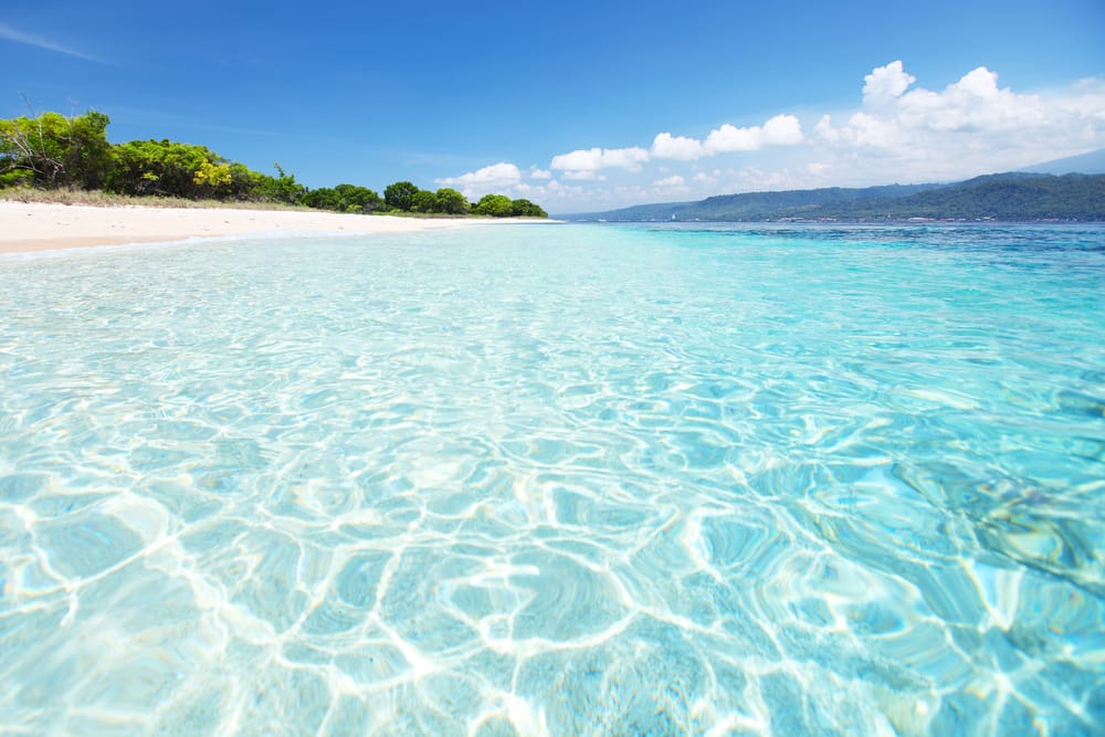 Den sandede kyst og det klare hav i Bali Barat Nationalpark nær Pemuteran – med udsigt over Javas kyst i horisonten.