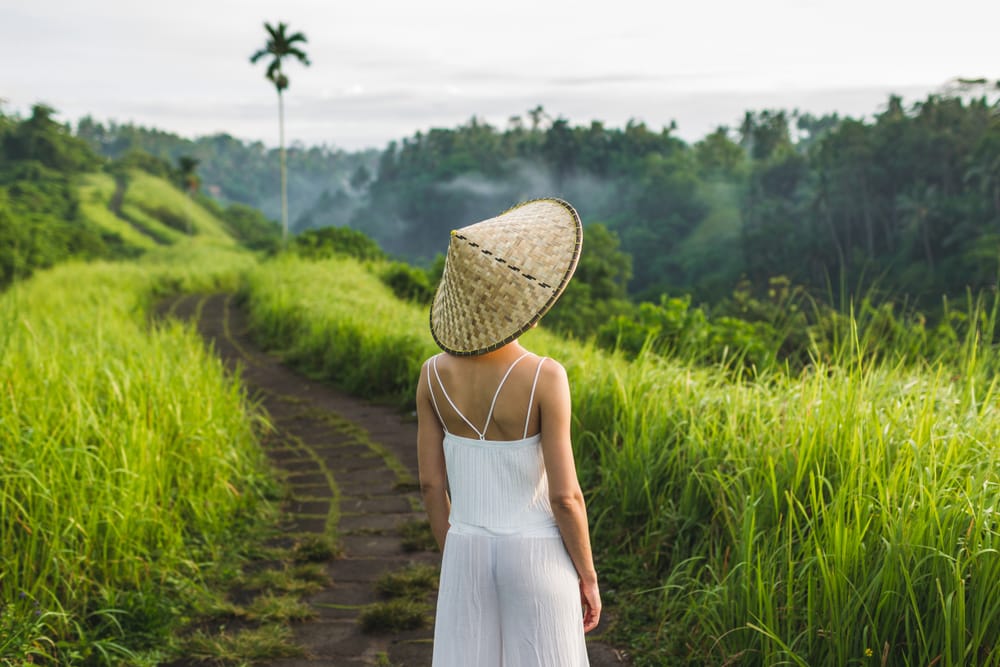 Ung kvinde går langs Campuhan Ridge Walk i Ubud, Bali, omgivet af grønne bakker og tropisk natur.