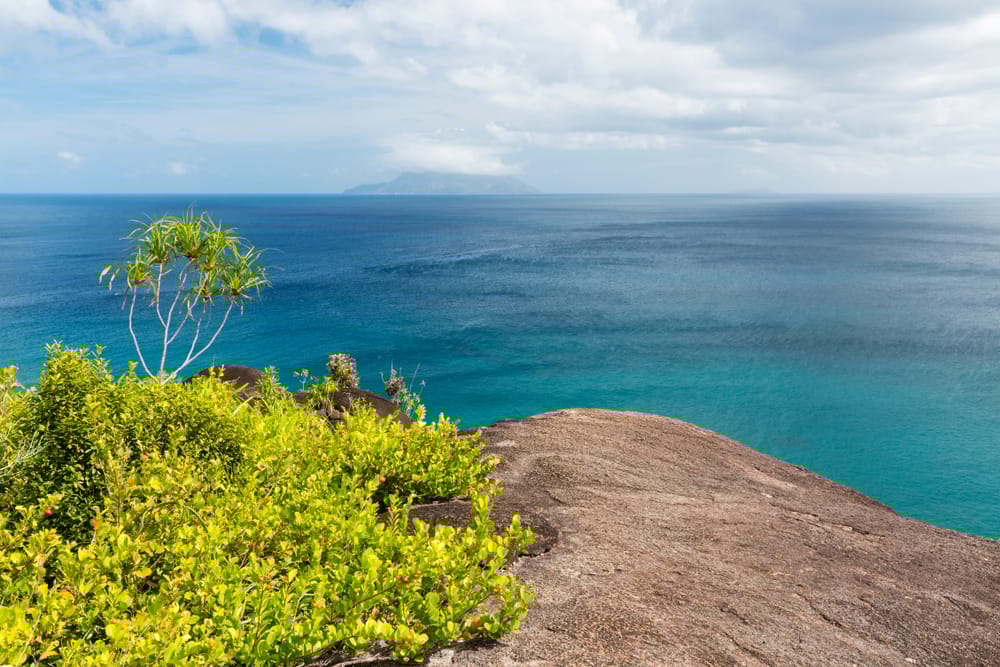 Udsigt fra Anse Major Trail på Mahé, Seychellerne med grønne bakker, klipper og klart turkisblåt hav langs vestkysten.