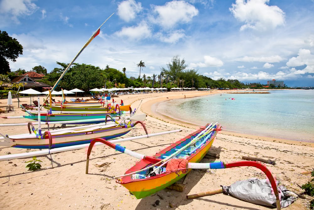 Traditionelle fiskerbåde på stranden i Sanur, Bali, Indonesien, med havet og morgensolen i baggrunden.