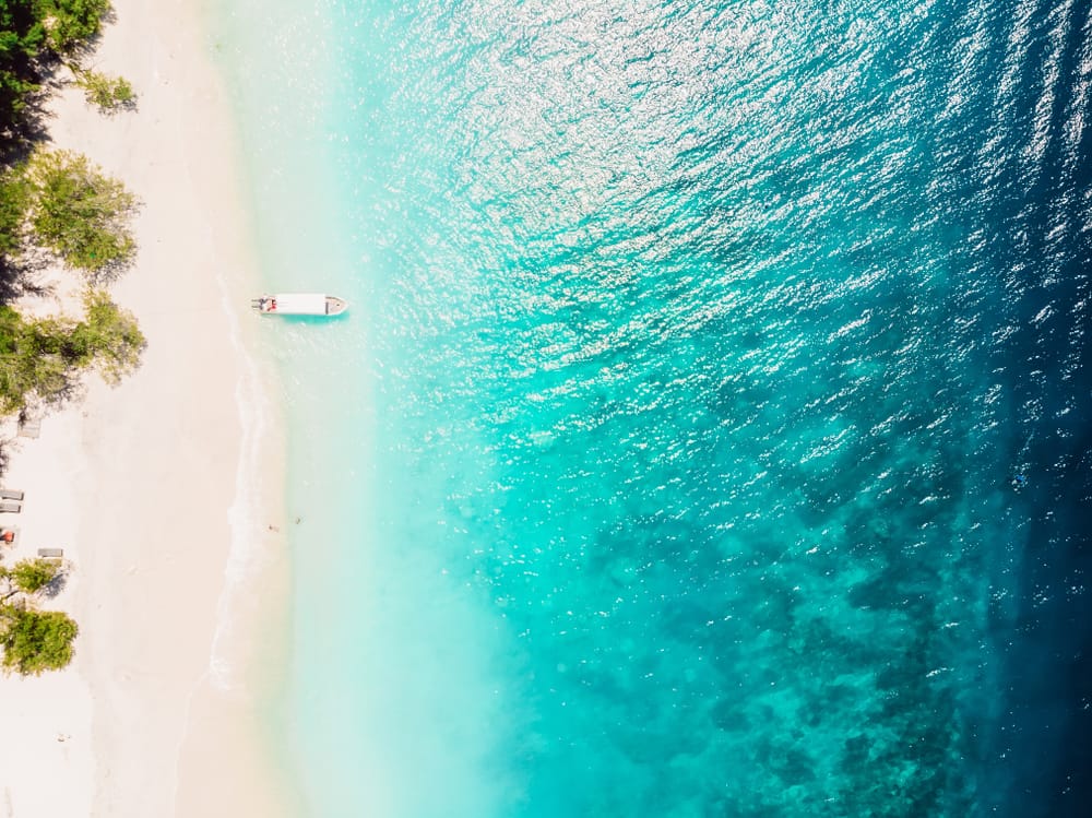 Luftfoto af tropisk strand ved Gili-øerne – turkisblåt hav, hvid sandstrand og svajende palmer i Indonesiens øparadis.