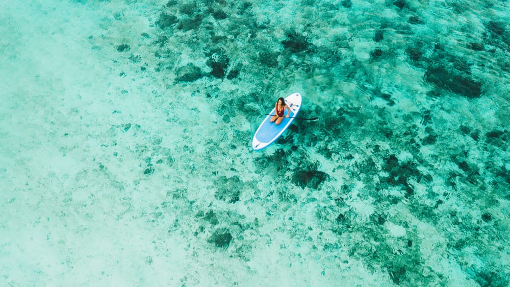 Kvinde på paddleboard i det krystalklare, turkisblå hav på Maldiverne.