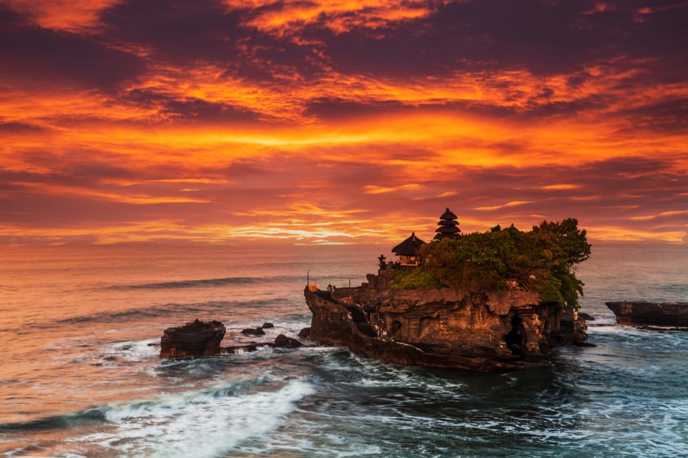 Tanah Lot Temple ved solnedgang på Bali, Indonesien, beliggende på en klippe omgivet af havet.
