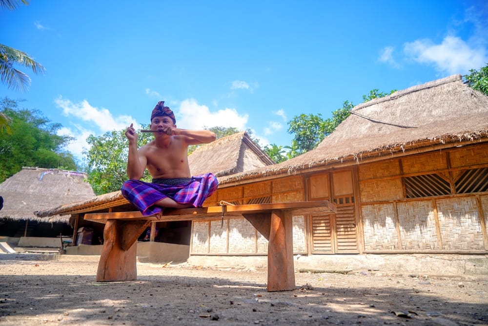 Mand i traditionel påklædning foran bambushuse i en Sasak-landsby på Lombok, Indonesien.