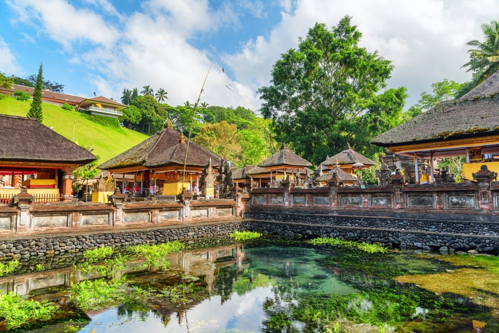 Hellig dam ved Tirta Empul-templet på Bali, Indonesien, omgivet af grøn natur og balinesisk arkitektur.