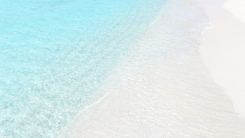Top-down billede af en maldivisk strand med hvidt sand og klart, lavt vand langs kysten.