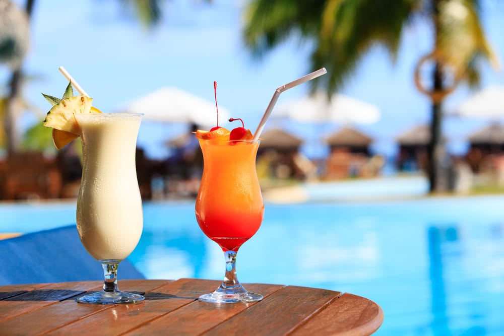 Farverige drinks ved en pool med udsigt over det turkisblå hav.