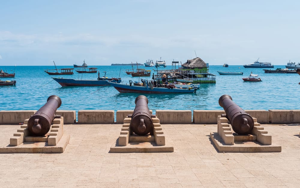 Kystpromenaden i Stone Town på Zanzibar med historiske kanoner og udsigt til både, der vugger i havet ud for byen.