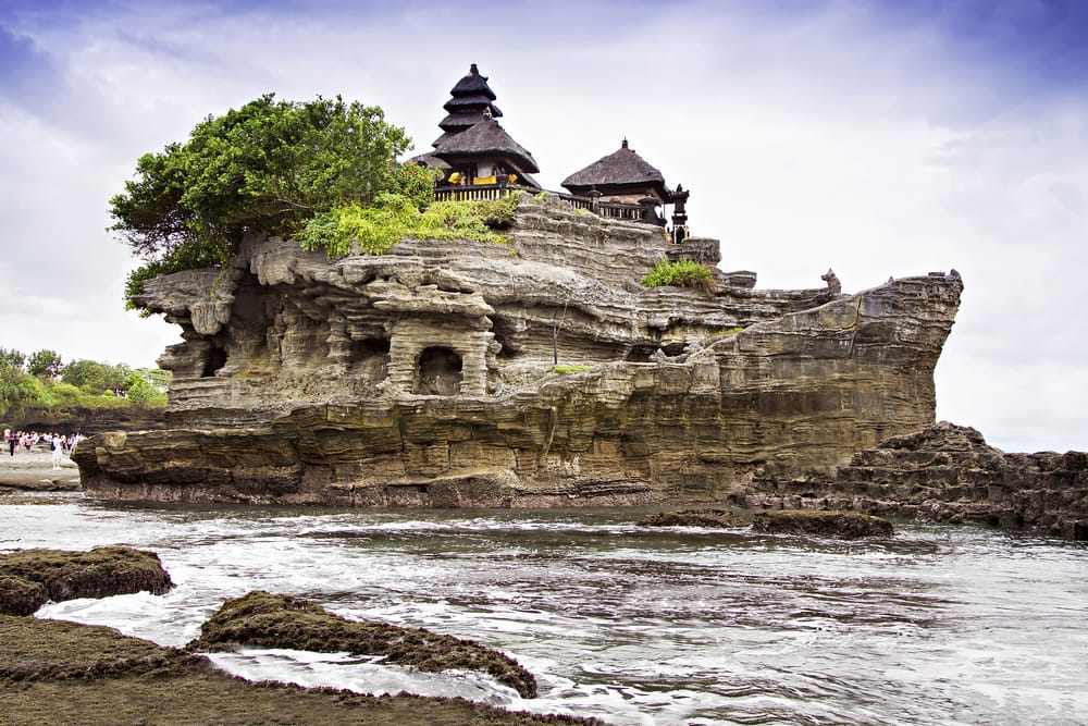 Tanah Lot-templet på Bali – et ikonisk havtempel bygget på en klippe omgivet af brusende bølger og gyldent sollys.