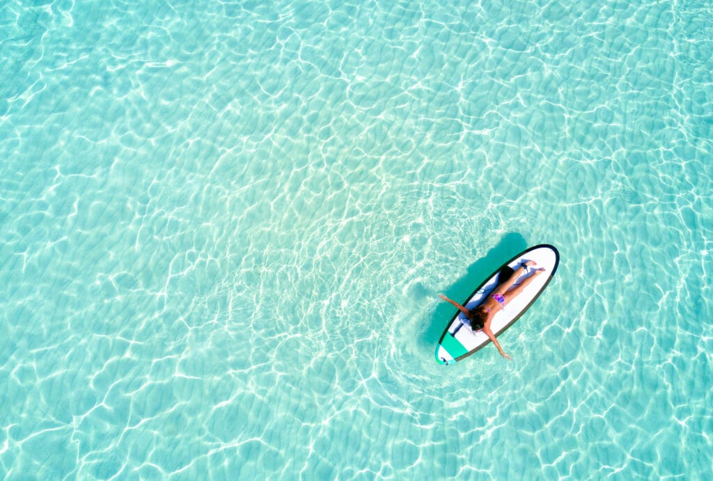 Kvinde ligger og slapper af på et paddleboard i det lavvandede, turkisblå vand ved Kandima Maldives
