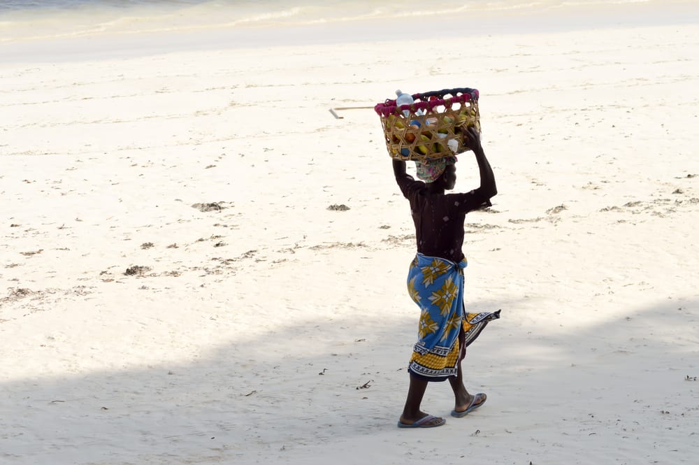 Lokal kvinde sælger mangoer på den solrige sandstrand ved Bamburi Beach nær Mombasa.