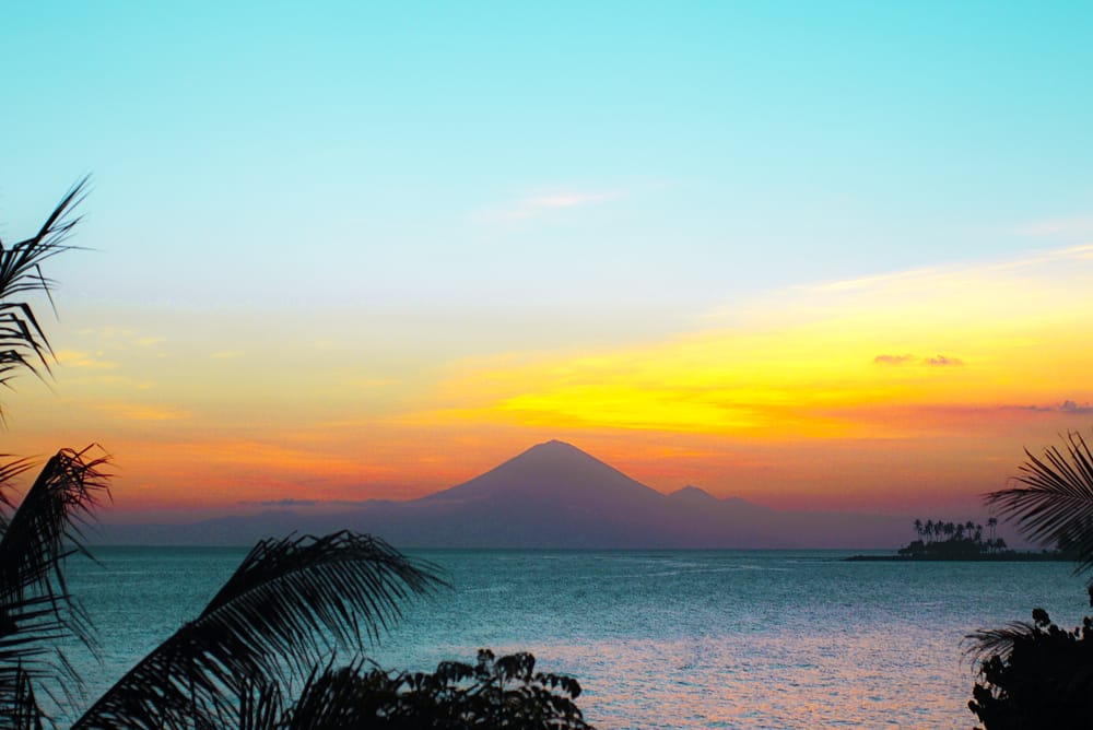 Solnedgang ved Senggigi Beach, Lombok, Indonesien, med palmer, hav og gyldne nuancer på himlen.