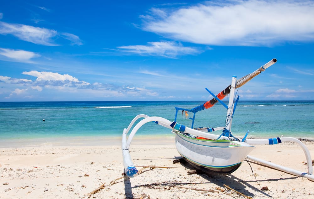 Traditionel fiskerbåd på stranden på Gili Trawangan, Indonesien, med turkis hav og palmer i baggrunden.