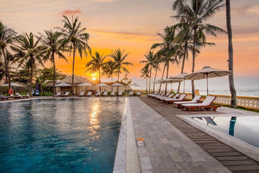 Poolområde ved strandresort i Vietnam med palmer og solnedgang i baggrunden.