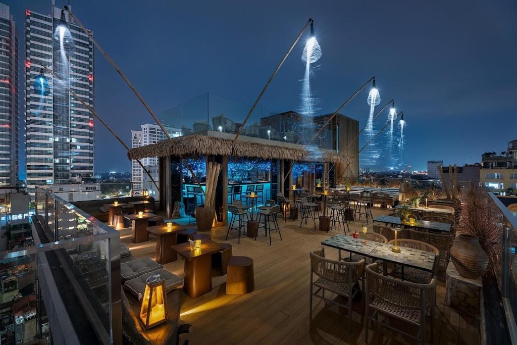 Rooftop bar i Hanoi om aftenen med udsigt over byens skyline og stemningsfulde lamper.