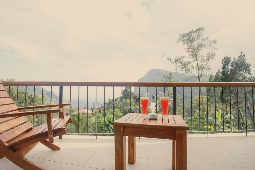 Terrasse med træstole og bord med to drinks og udsigt over grønt højlandslandskab og bjerge i Ella, Sri Lanka.