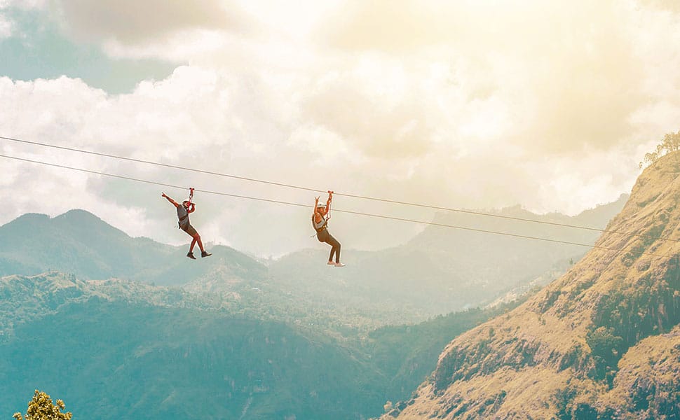Person svæver i zipline over frodigt højlandslandskab ved Flying Ravana i Ella, Sri Lanka.