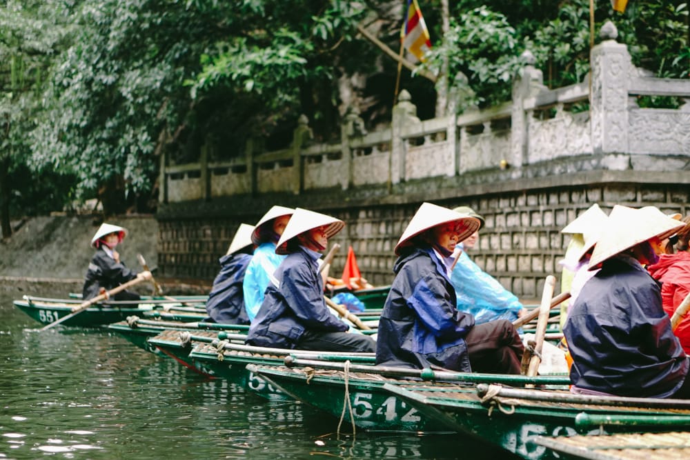 Sampanbåd sejler gennem huler i Trang An, Ninh Binh, omgivet af kalkstensbjerge og frodig natur