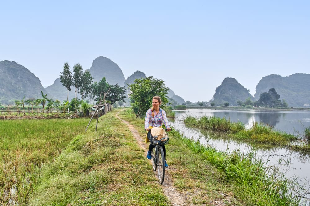 Kvinde der cykler gennem rismarker ved Nin Binh