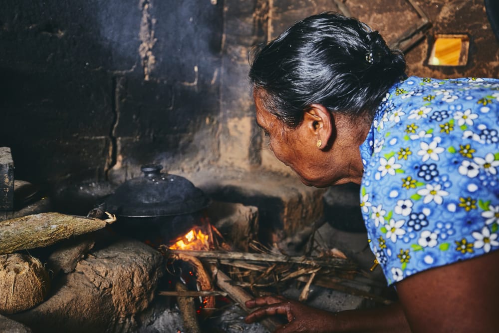 Kvinde tilbereder mad i et traditionelt srilankansk køkken med enkle redskaber og lerpotter.