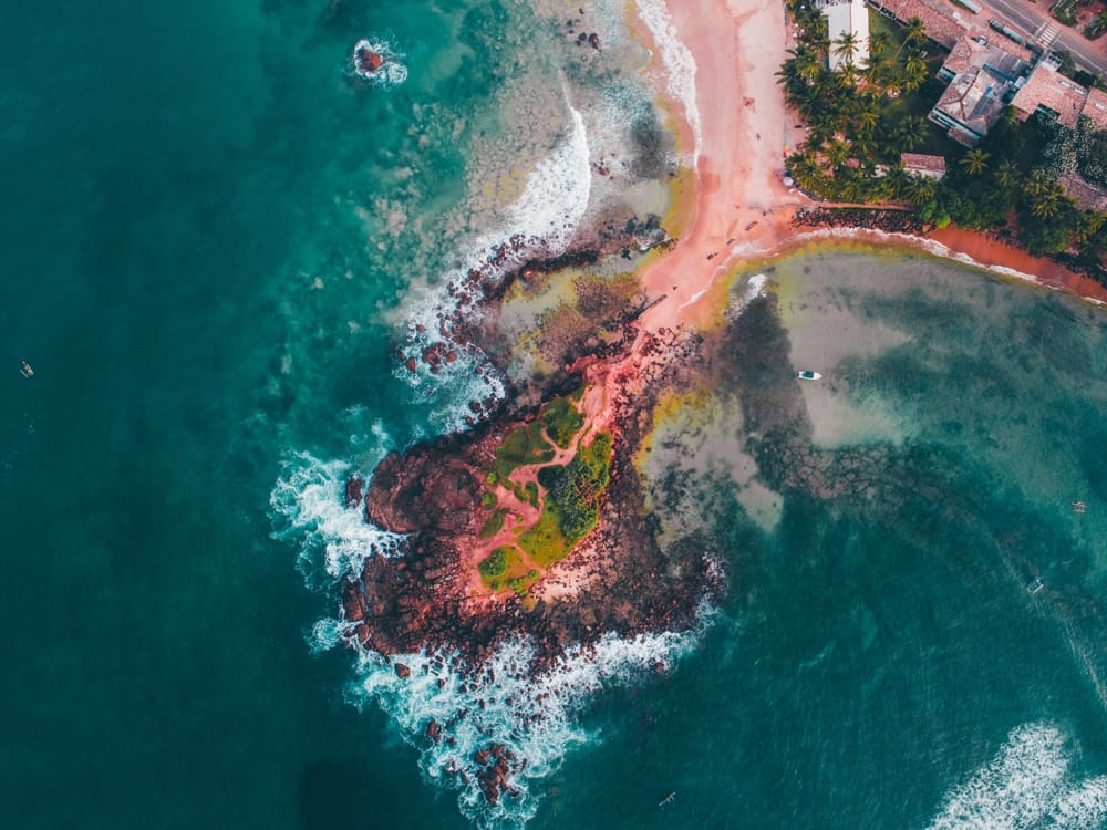 Luftfoto af Mirissa i Sri Lanka med sandstrand, palmer, kystby og det blå ocean set fra oven.