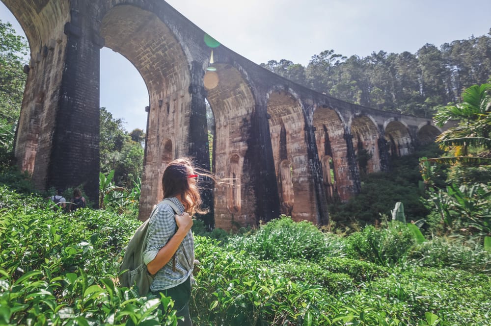 Kvinde står med udsigt over Nine Arches Bridge ved Ella, omgivet af grøn jungle og bakkelandskab.