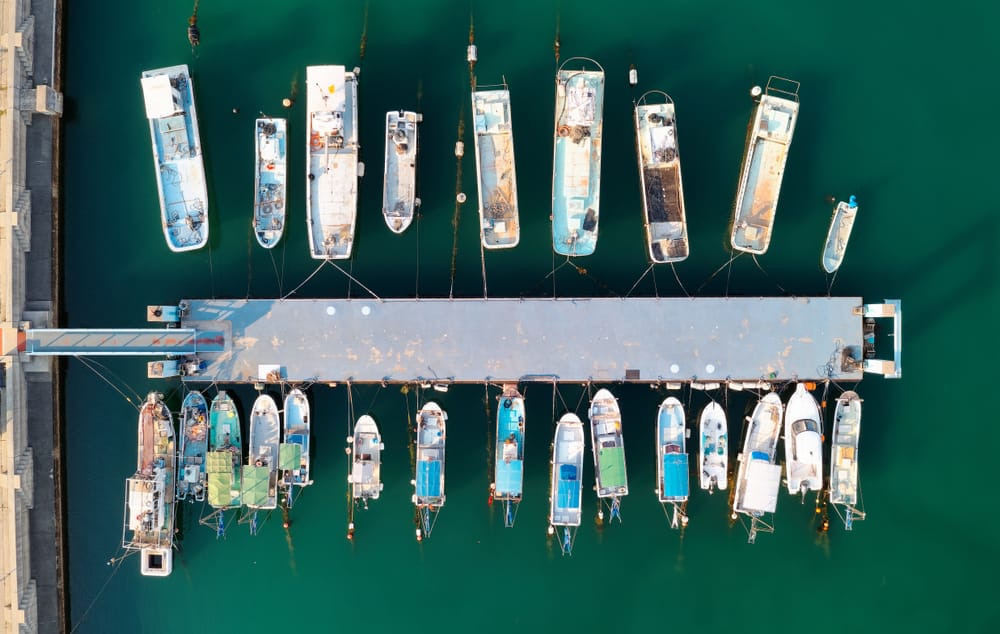 Aerial view of fishing boats and yachts moored in Naoshima Island harbor, Kagawa, Japan, with clear green water and sunny summer light.