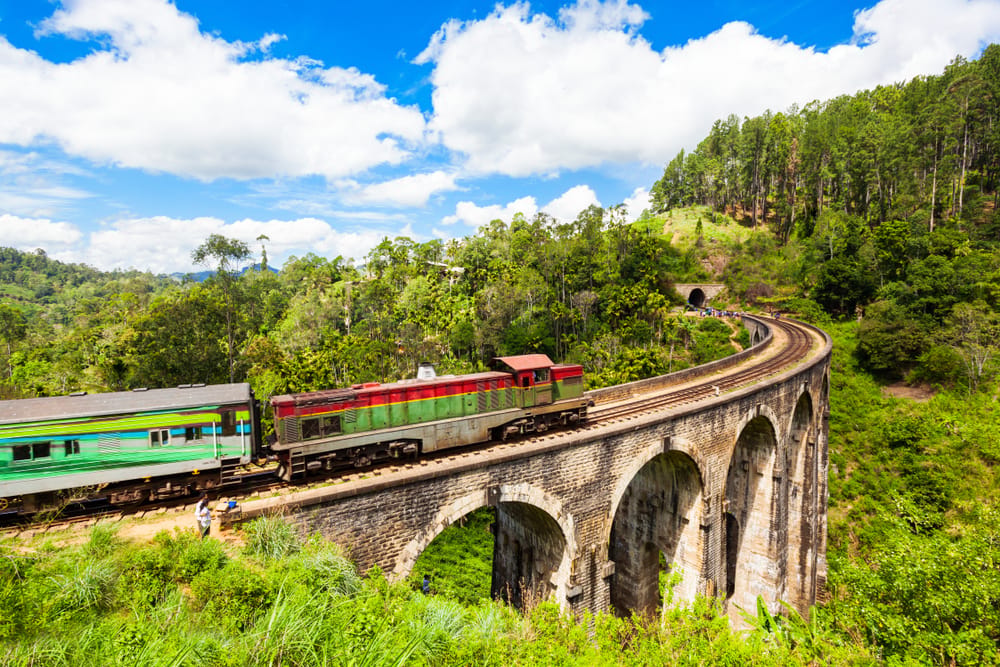 Tog kører over Nine Arches Bridge ved Ella, en historisk stenbro med ni buer omgivet af grøn jungle.