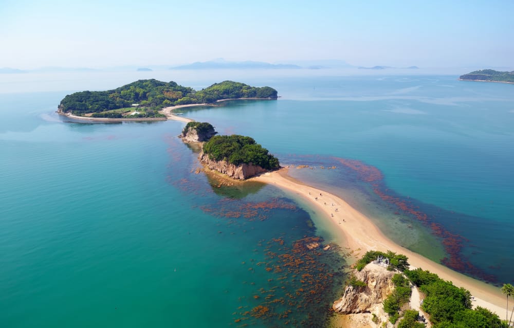 Aerial view of Angel Road on Shōdoshima Island in Japan, with a sandy land bridge surrounded by turquoise water and a bright blue sunny sky.