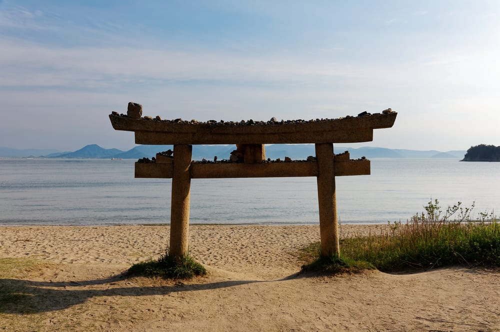 Rød torii-port ved Seto-indhavet på en solrig sommerdag med blåt hav, himmel og fredfyldt japansk kystlandskab.