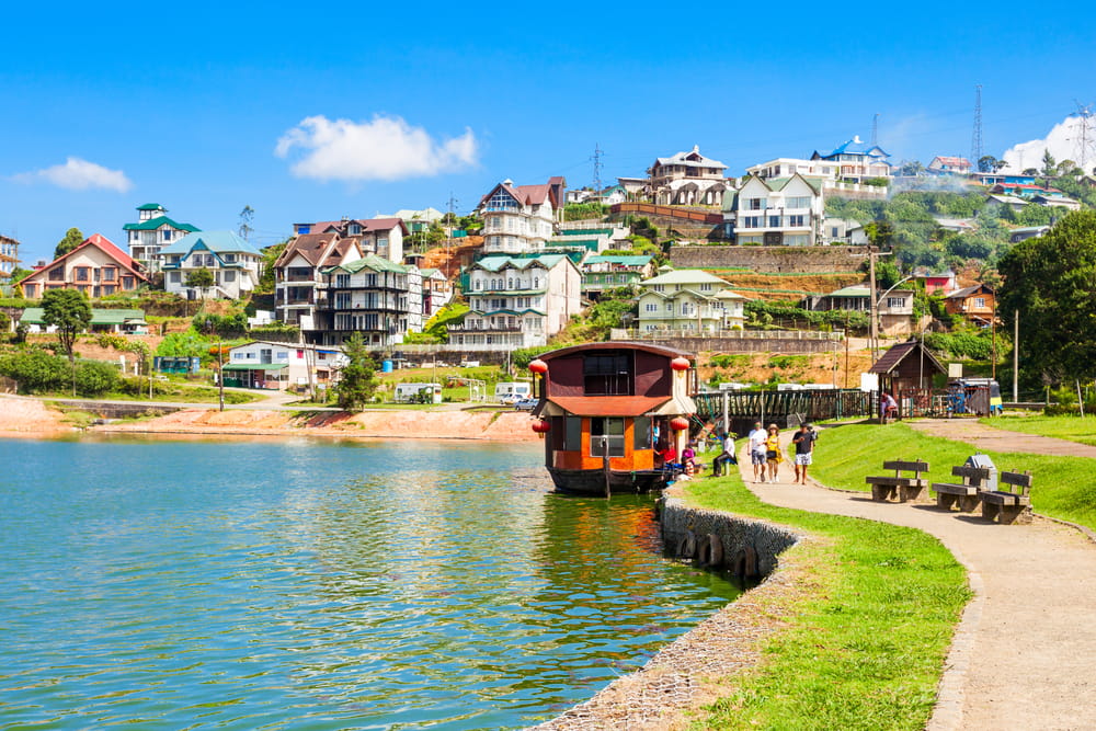 Husbåd på Gregory Lake i Nuwara Eliya med bjerge og grønne omgivelser i baggrunden.